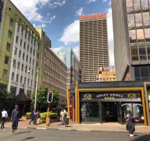 Street intersection in the Johannesburg CBD with pedestrians, traffic lights, and city buildings.