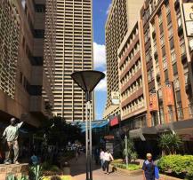 Urban street scene with landscaped planters, people walking, and tall business buildings.