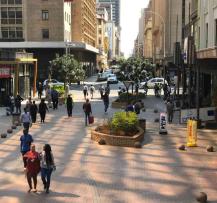 Pedestrian mall lined with shops, trees, and outdoor seating on a sunny day.