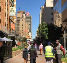 People walking along Fox Street with shading patterns cast by surrounding tall buildings.